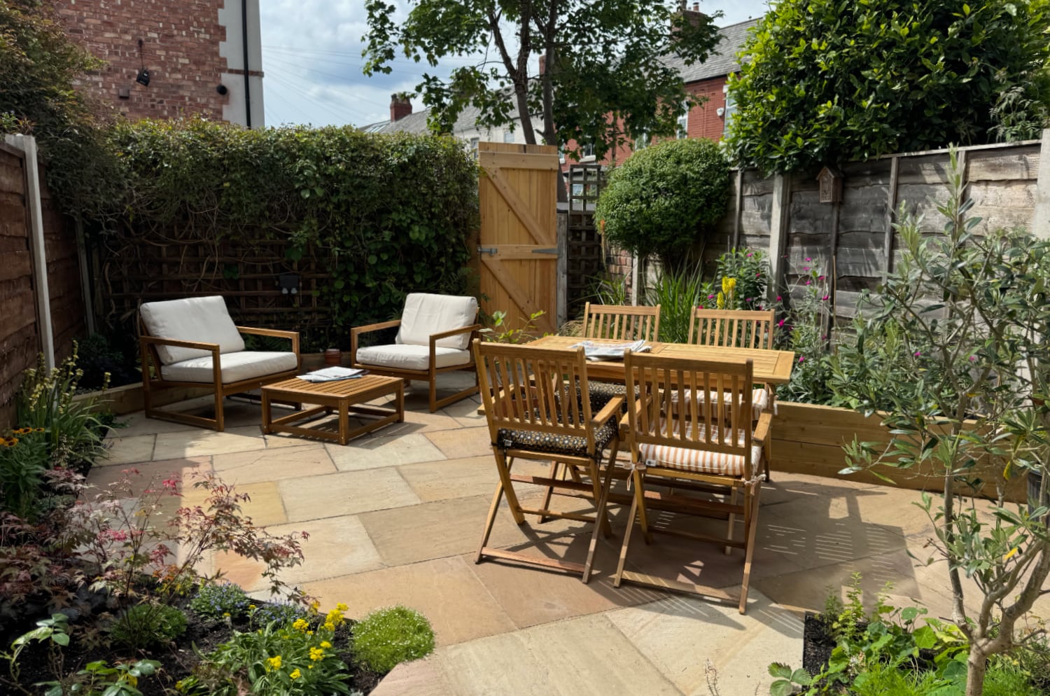 A partially paved garden with triangular beds to the left and right, and garden furniture