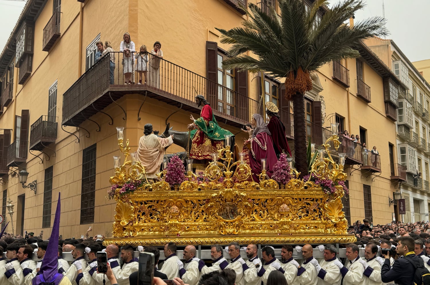 A gold float with Jesus on a donkey being carried by dozens of robed men through the streets of Malaga